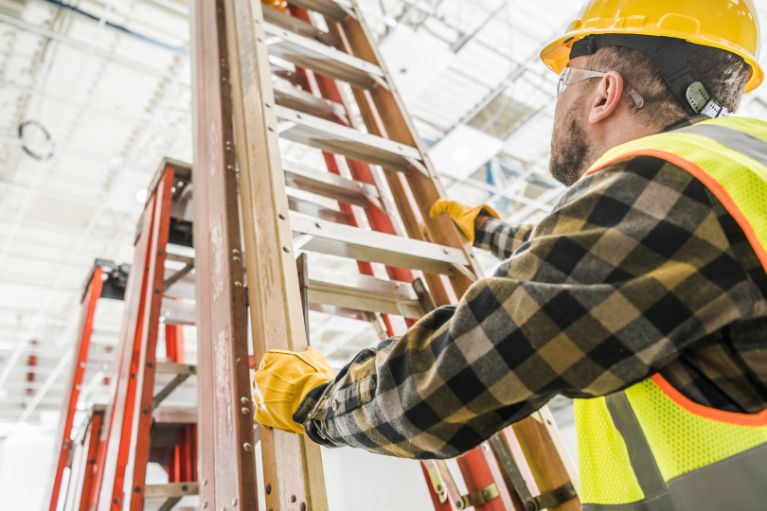 Tools and equipment training and safety course illustrating a man in a high visual jacket and safety helmet positioning step ladders safely